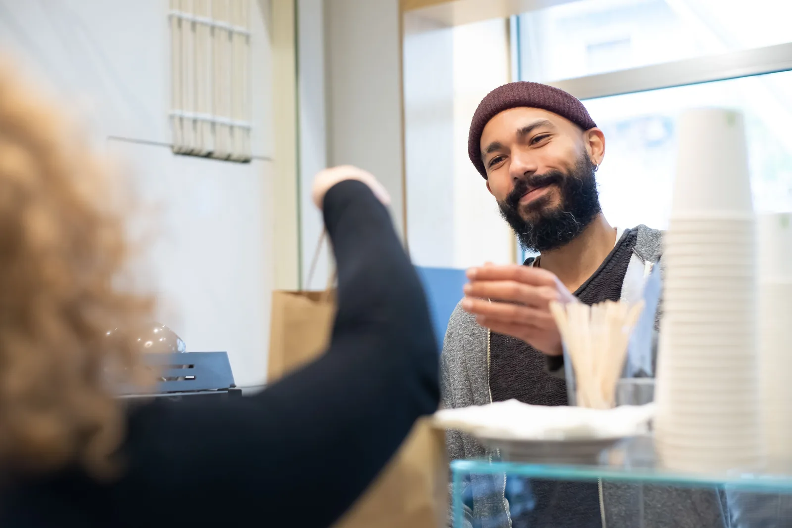 A small business owner in an apron handing a bag to a customer across the shop counter